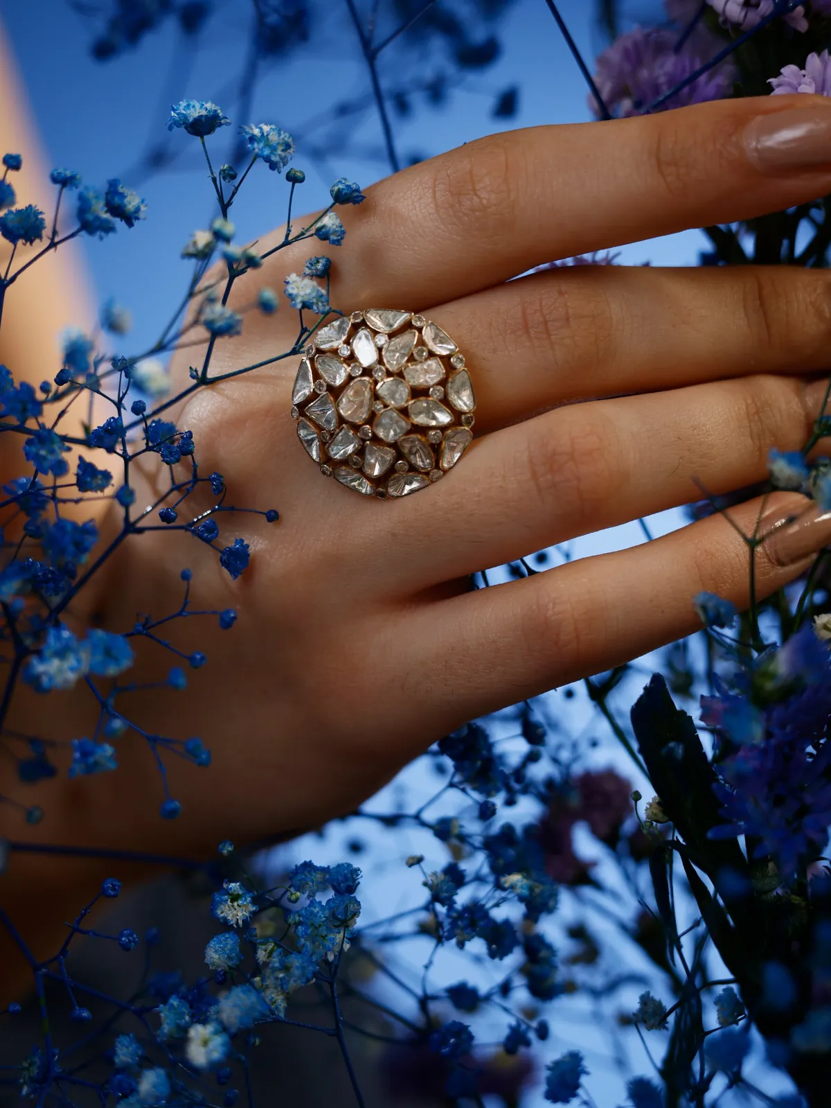 Polki cocktail ring on a hand among blue flowers